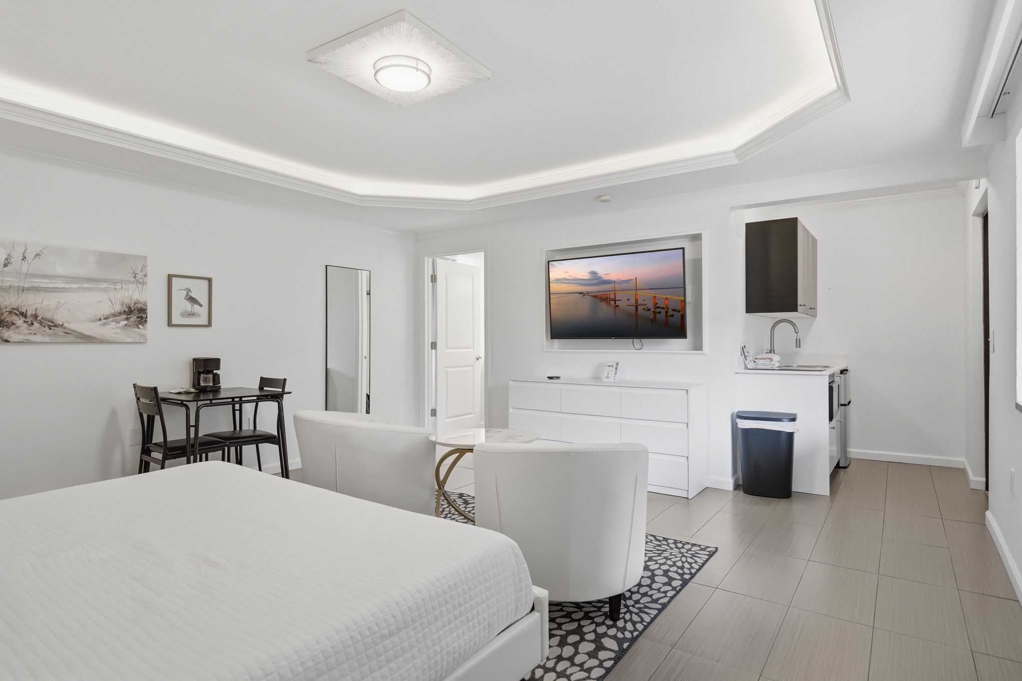 Habitación de hotel moderna con una cama grande, un escritorio con una silla, un tocador con espejo y un televisor.