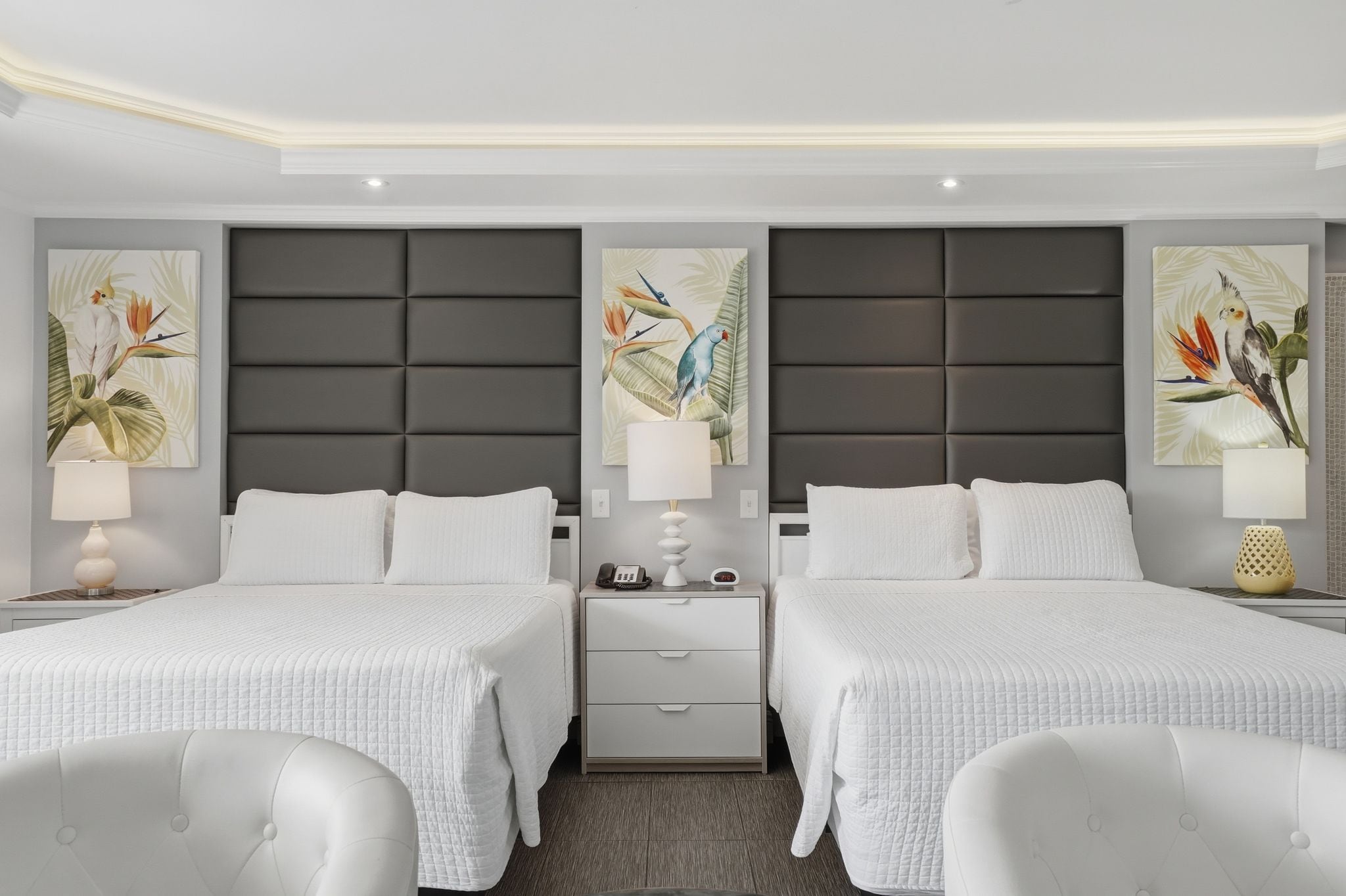 A hotel room with two beds, a large padded headboard, and artwork on the walls.
