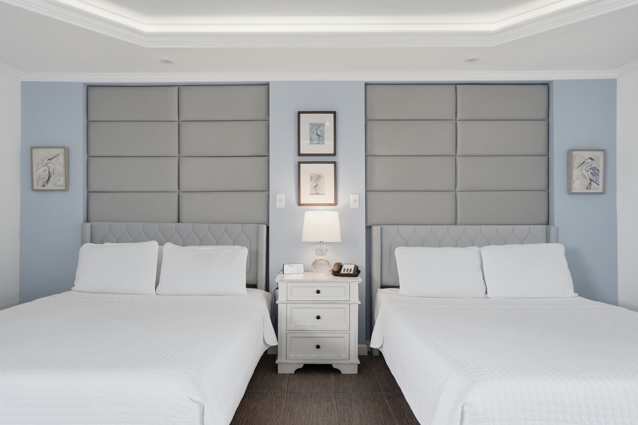A hotel room with two beds, a nightstand with a lamp, and artwork on the walls.