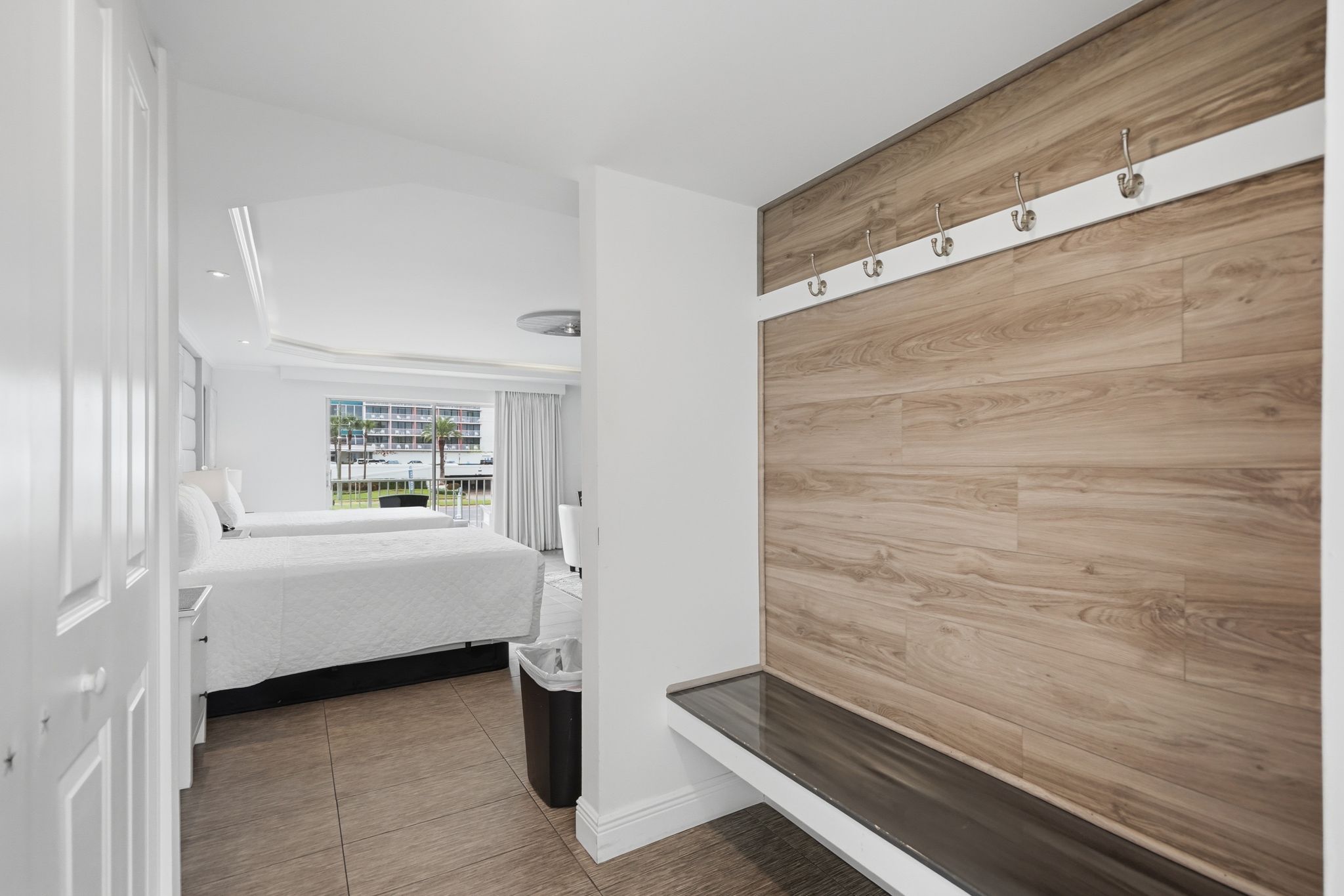 Quarto de hotel com uma cama, um painel de parede em madeira, uma janela com vista e uma lixeira.