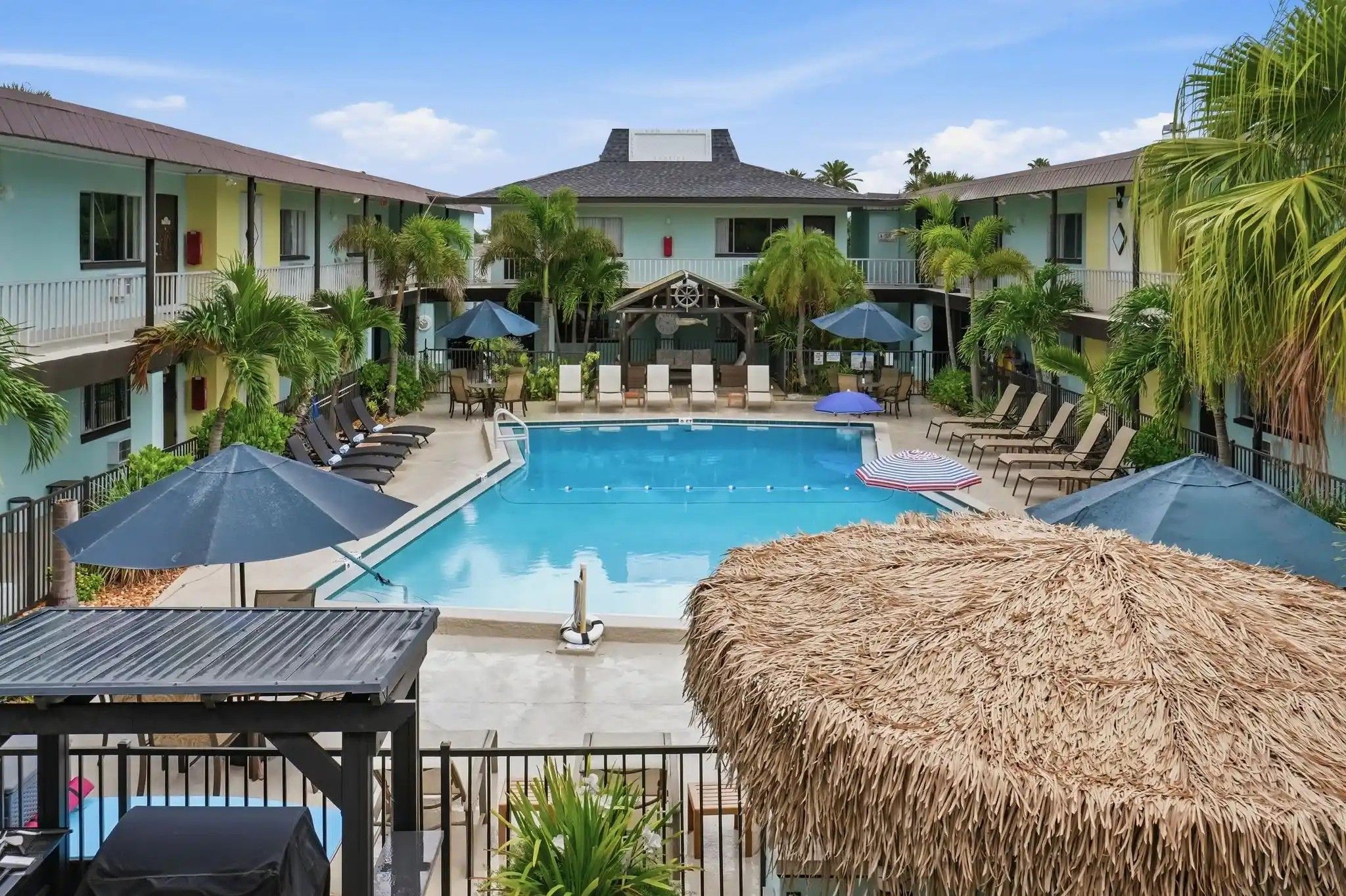 A pool area with lounge chairs and umbrellas, surrounded by buildings with balconies.