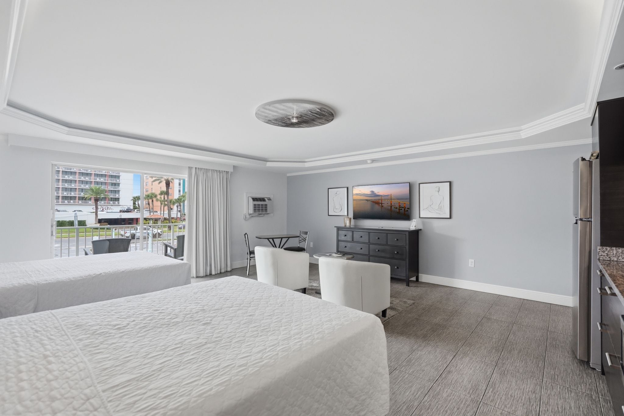 A hotel room with two beds, a desk, a television, and a view of the city.