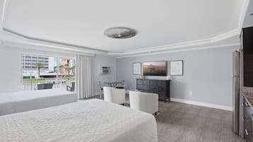 A hotel room with two beds, a desk, a television, and a view of the city.