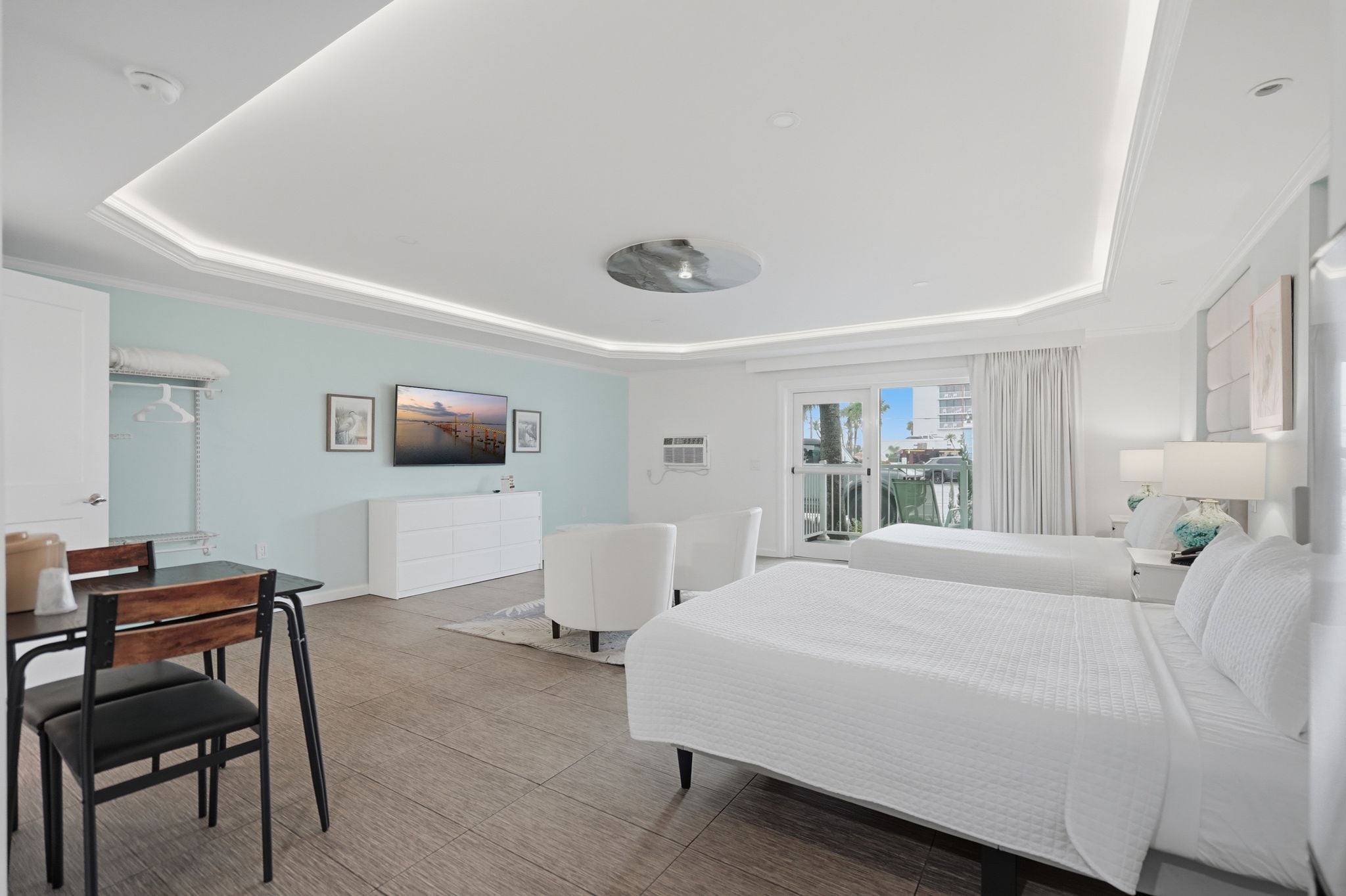 A hotel room with a bed, a desk, a chair, a wardrobe, and a view of the outside.