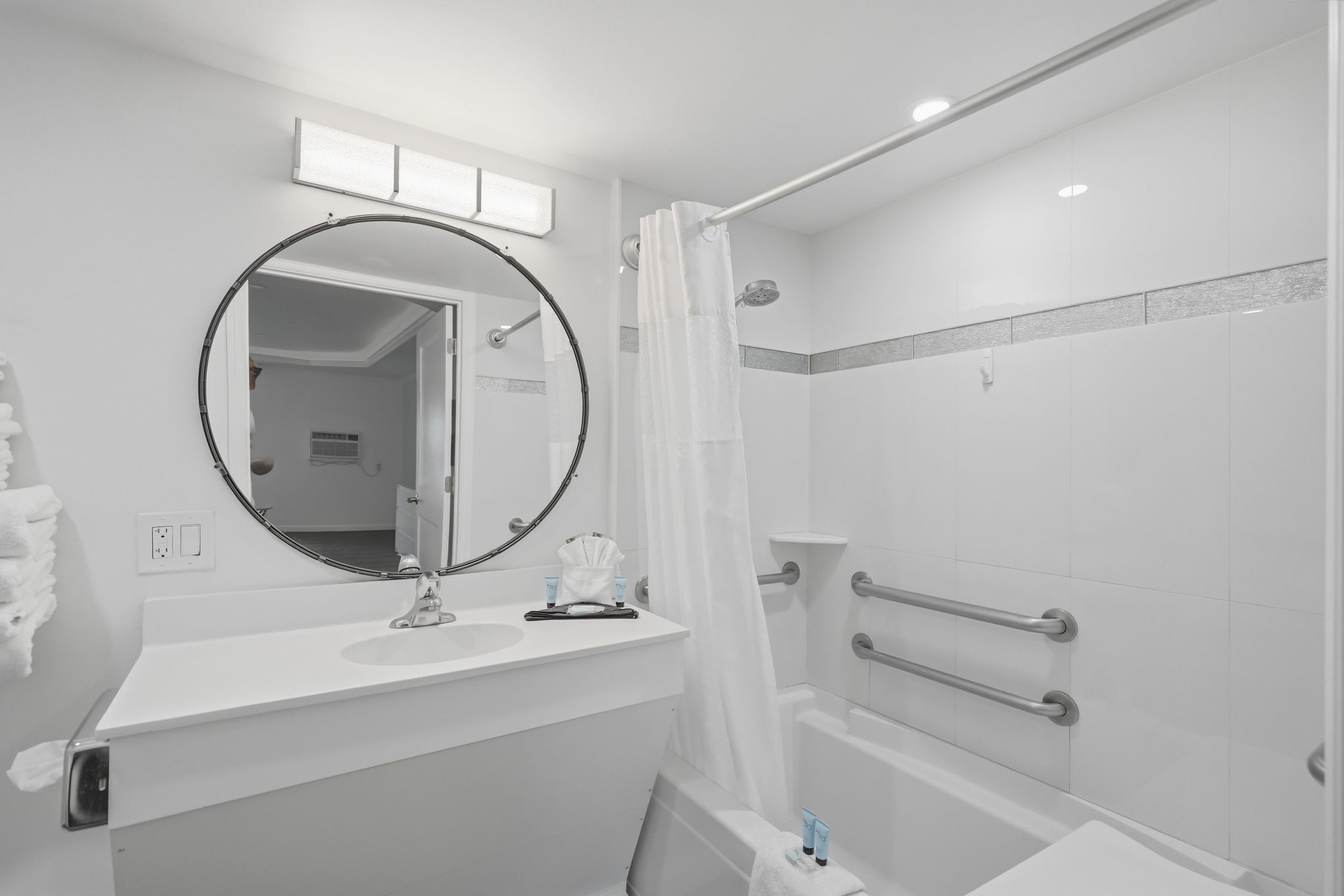 Une salle de bain moderne avec un miroir rond, une douche dotée d’une porte en verre et un lavabo blanc.