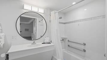 Une salle de bain moderne avec un miroir rond, une douche dotée d’une porte en verre et un lavabo blanc.