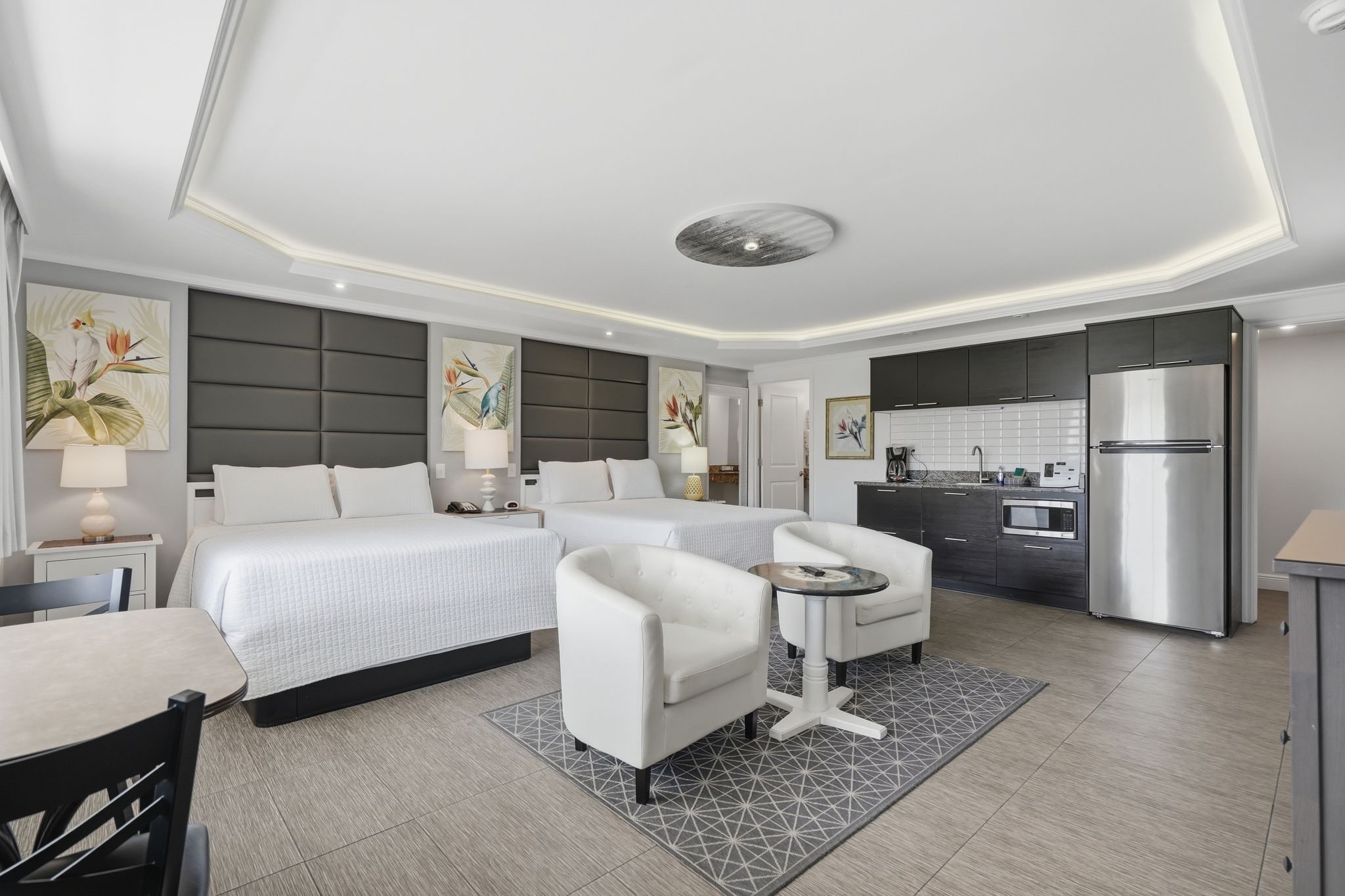 Una habitación de hotel con una cama, dos mesitas de noche, un sofá, una pequeña mesa de comedor y una kitchenette equipada con refrigerador y microondas.