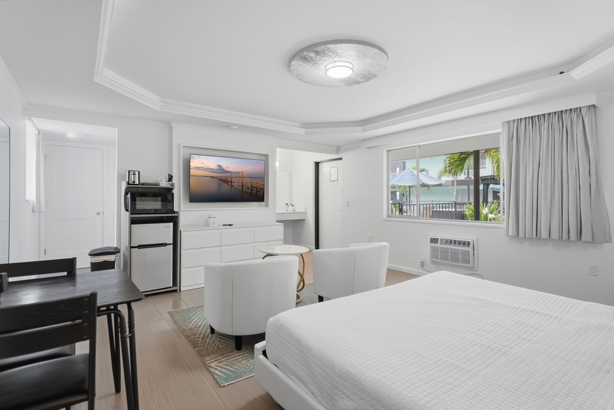 Une chambre d’hôtel comprenant un lit, un bureau, une chaise, une télévision, un minibar et une fenêtre avec des rideaux.