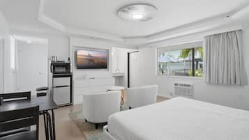Habitación de hotel con cama, escritorio, silla, televisor, minibar y ventana con cortinas.