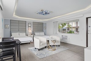 A hotel room with a bed, two white sofas, a small table, a chair, and a window with a view of a building and trees. - Island House Hotel (North Redington Beach)