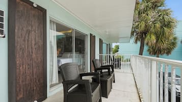 A balcony with outdoor furniture, a view of the interior, and a palm tree.