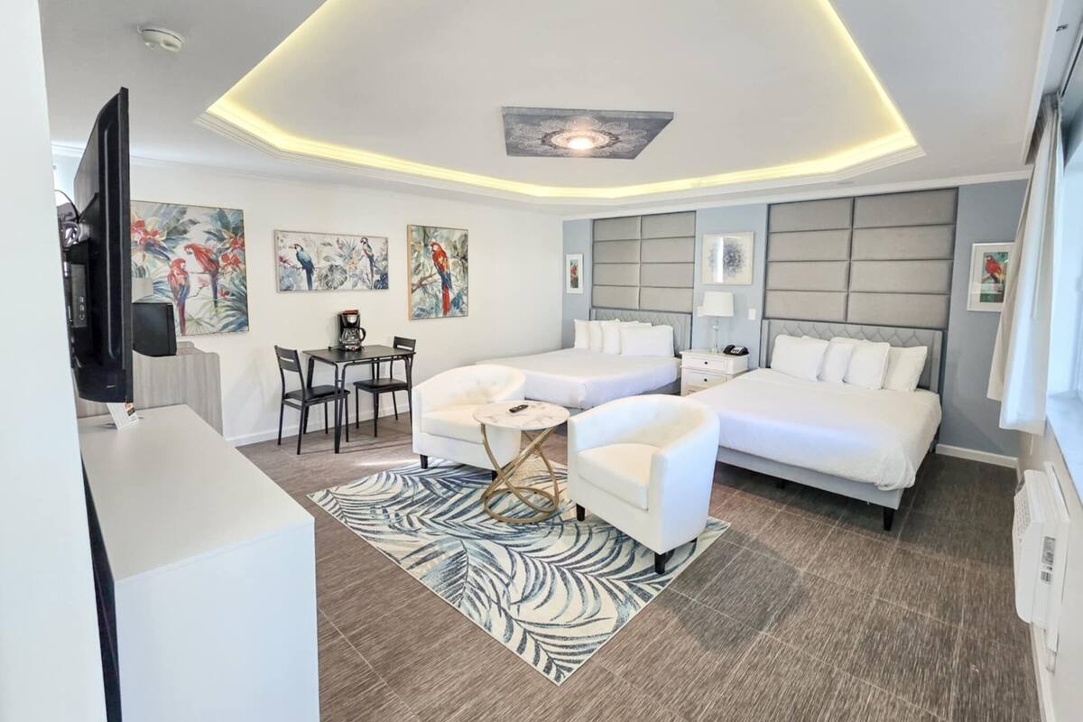 A modern hotel room with a large bed, a smaller bed, a desk with a chair, a TV, and artwork on the walls.