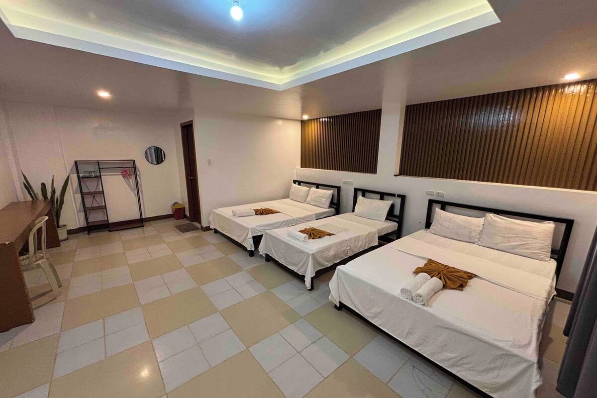 A hotel room with three beds, a desk, and a chair.