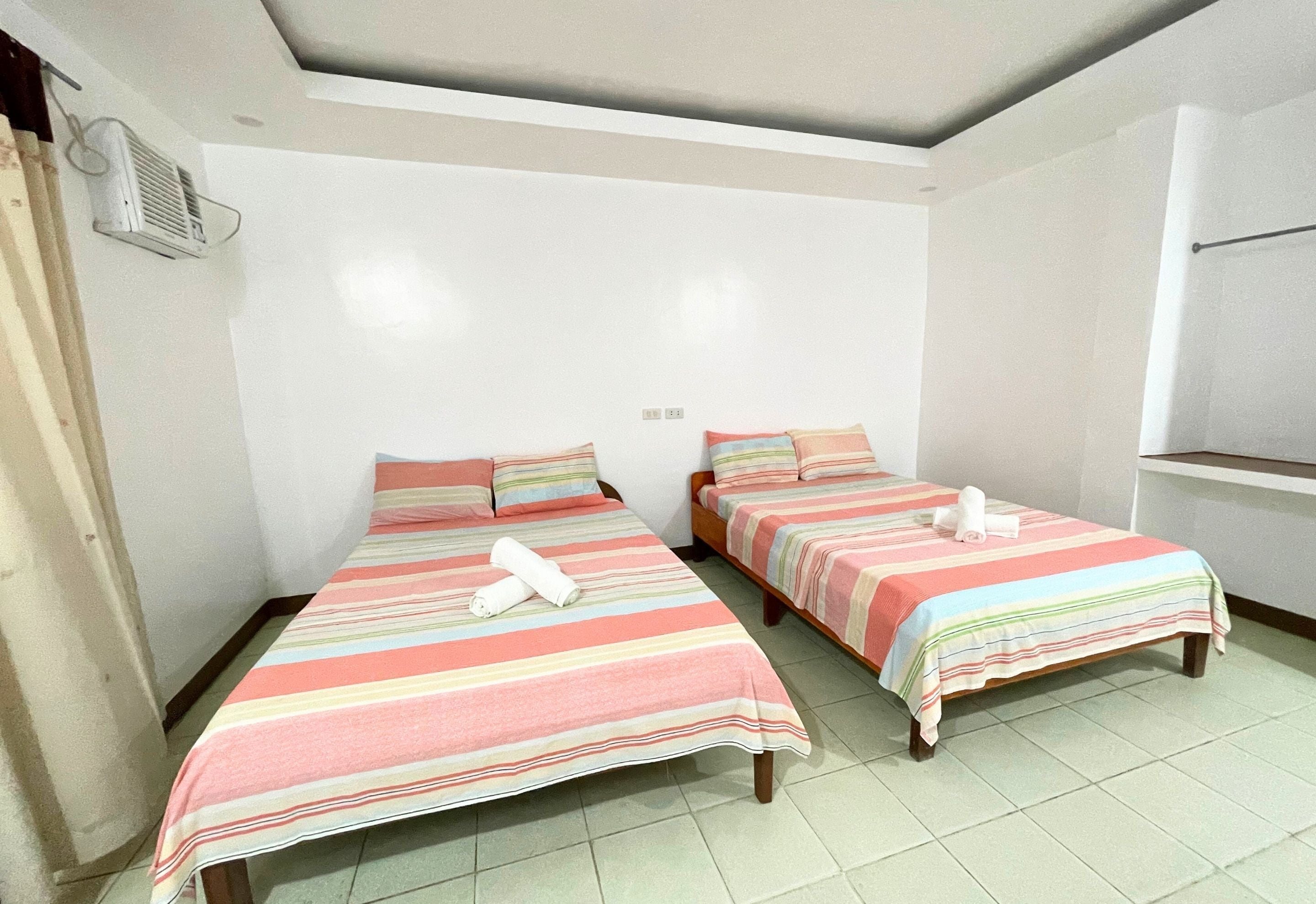 Two single beds with striped bedding, a ceiling fan, and a window with curtains.