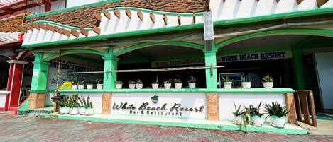 The exterior of White Beach Resort Bar & Restaurant with a green and white facade, potted plants, and a signboard.
