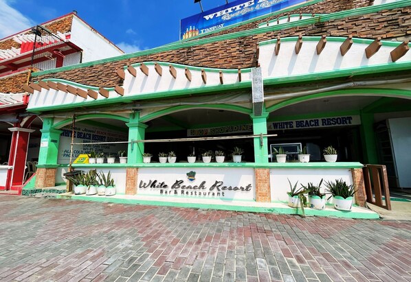 Exterior del Bar y Restaurante White Beach Resort, con fachada verde y blanca, plantas en macetas y un cartel.
