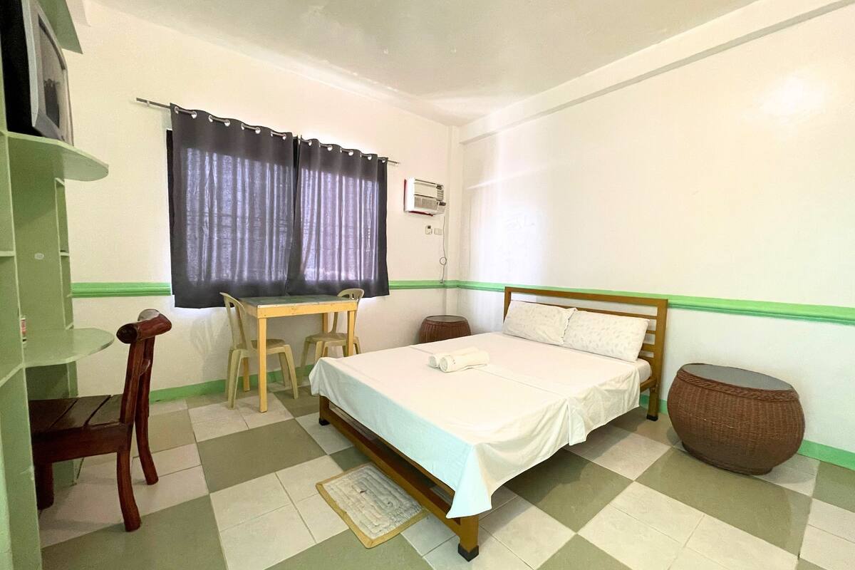 A bedroom with a bed, a desk, a chair, and a small round table.