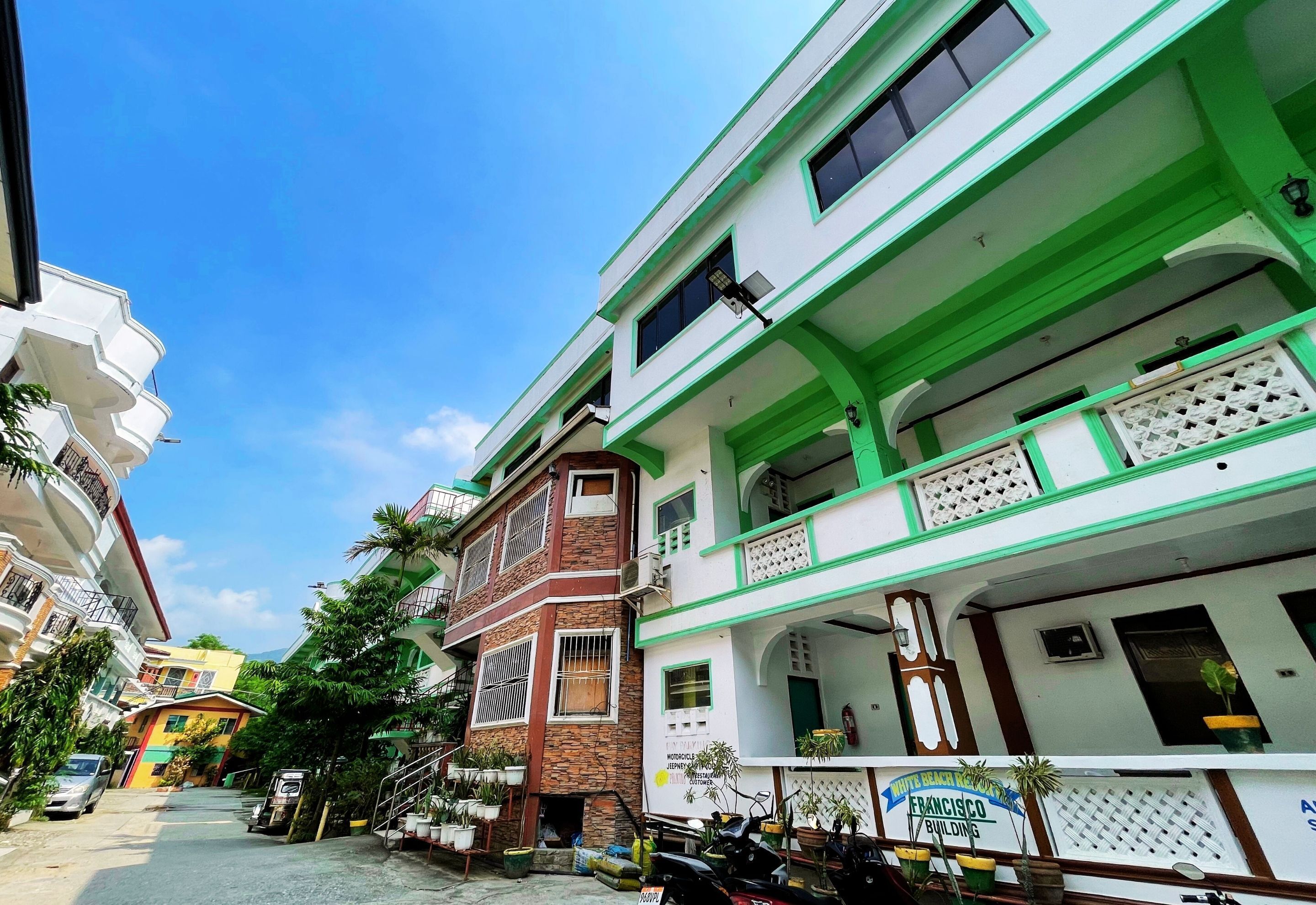 A multi-story building with a green and white facade, multiple balconies, and a sign indicating a hotel.