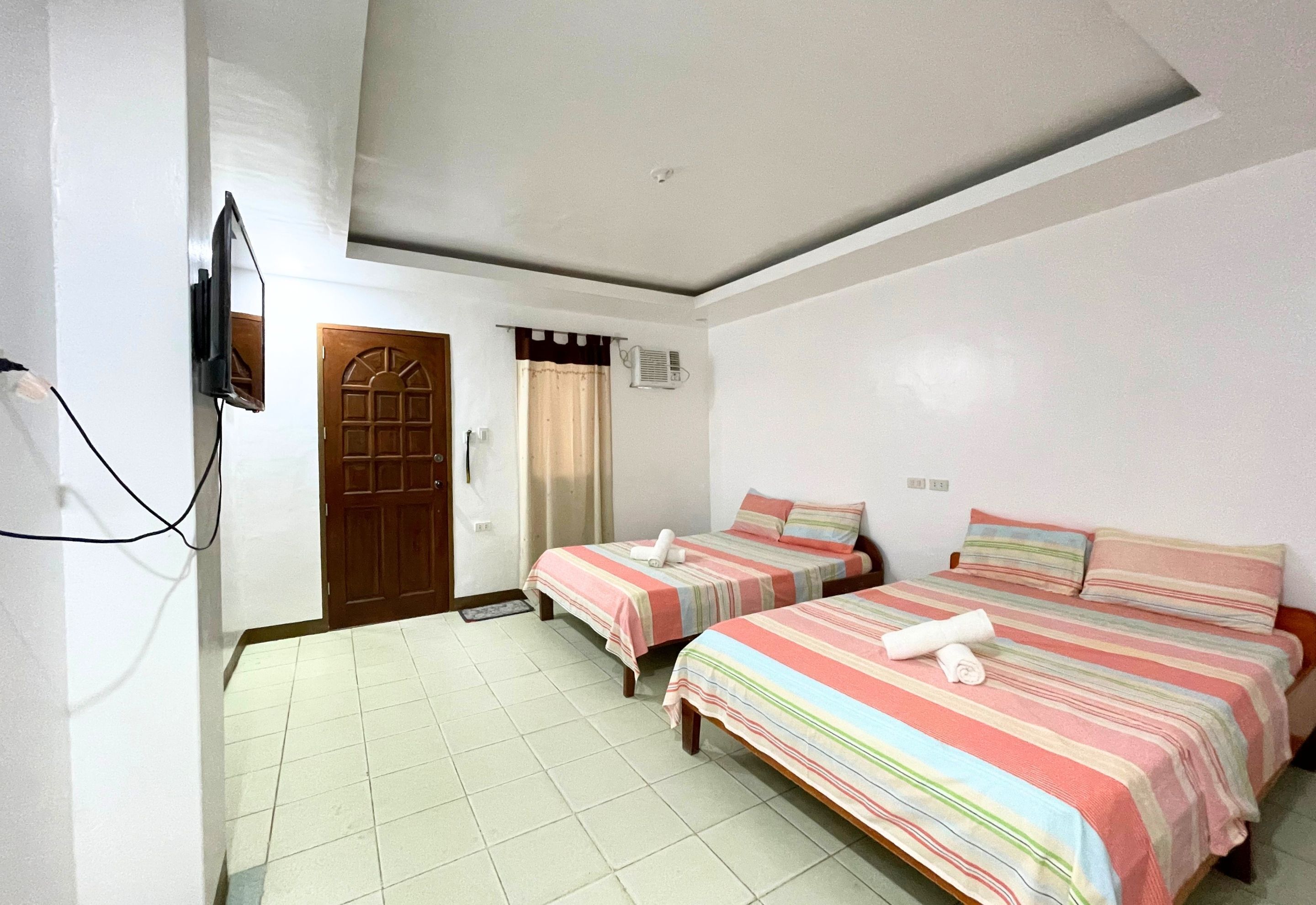Quarto de hotel com duas camas, uma televisão, uma porta e um ar condicionado.