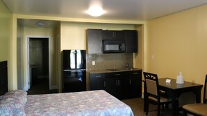 A hotel room with a bed, a small kitchenette, a dining table with chairs, and a bathroom door. - Crown Inn Motel (Yorktown)