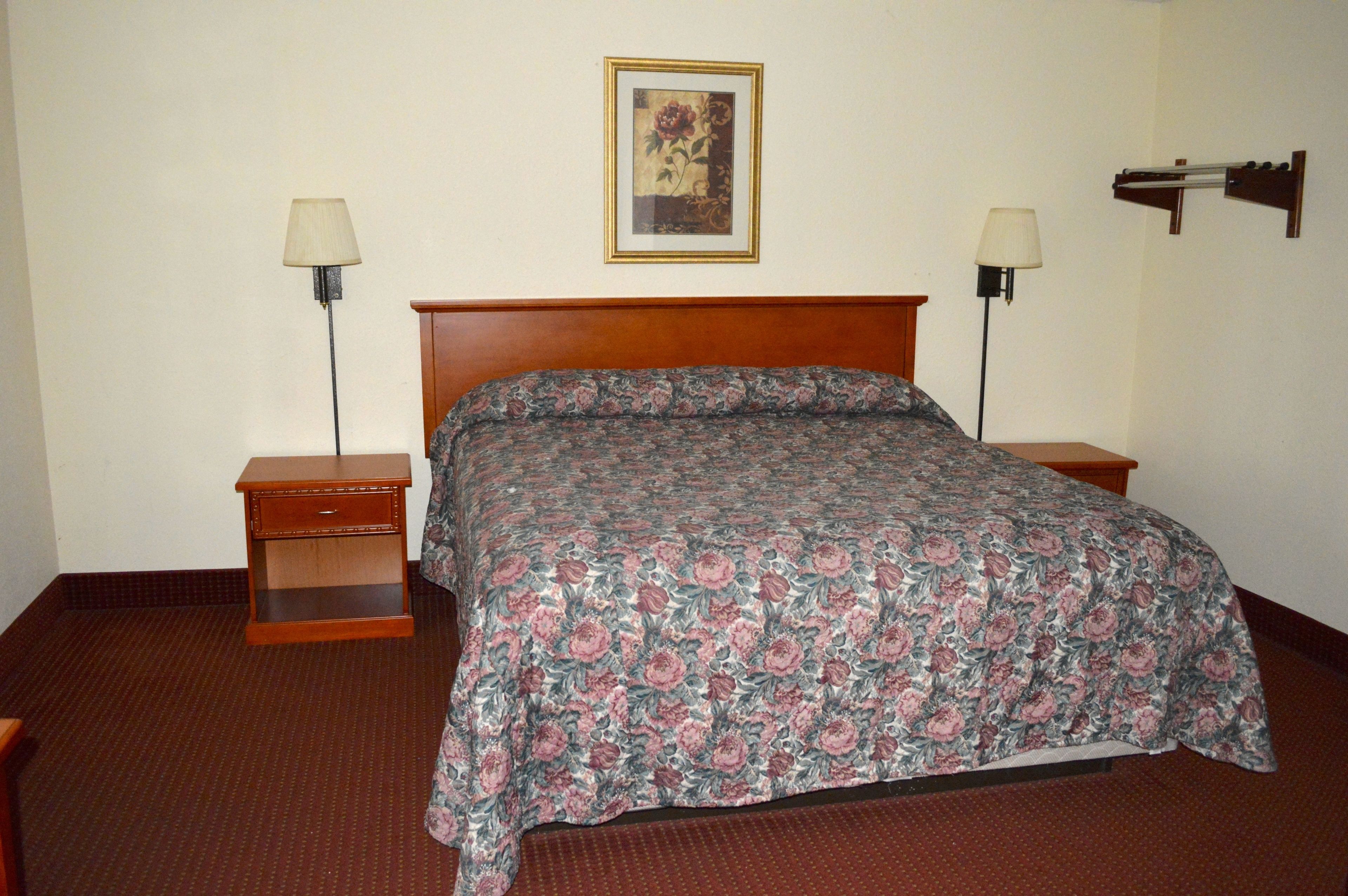 A hotel room with a wooden bed, floral bedspread, two bedside tables with lamps, and a framed picture on the wall.