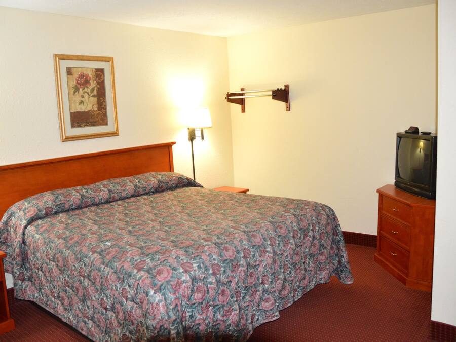 Habitación de hotel con cama, mesita de noche, lámpara, cómoda y televisor.