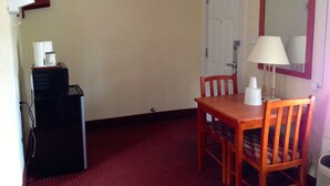 A small, simple room with a wooden table and chair, a white door, and a small heater on the floor. - Crown Inn Motel (Yorktown)