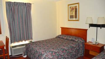 Ein Hotelzimmer mit Bett, Schreibtisch, Stuhl, Nachttisch mit Lampe und einem Fenster mit Vorhängen.