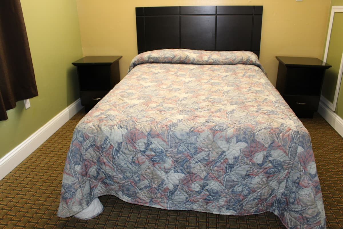 A neatly made bed with a floral bedspread, two bedside tables, and a dark headboard in a room with green walls and patterned carpet.