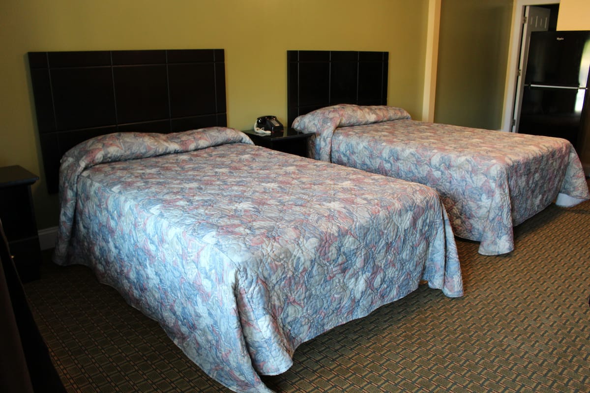 A hotel room with two beds, a nightstand, and a refrigerator.