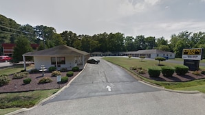 A Crown Inn with a simple, single-story structure, a parking lot, and a grassy area with trimmed bushes. - Crown Inn Motel (Yorktown)