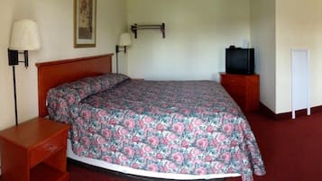 A hotel room with a single bed, a nightstand, a TV on a stand, and a wall-mounted lamp.
