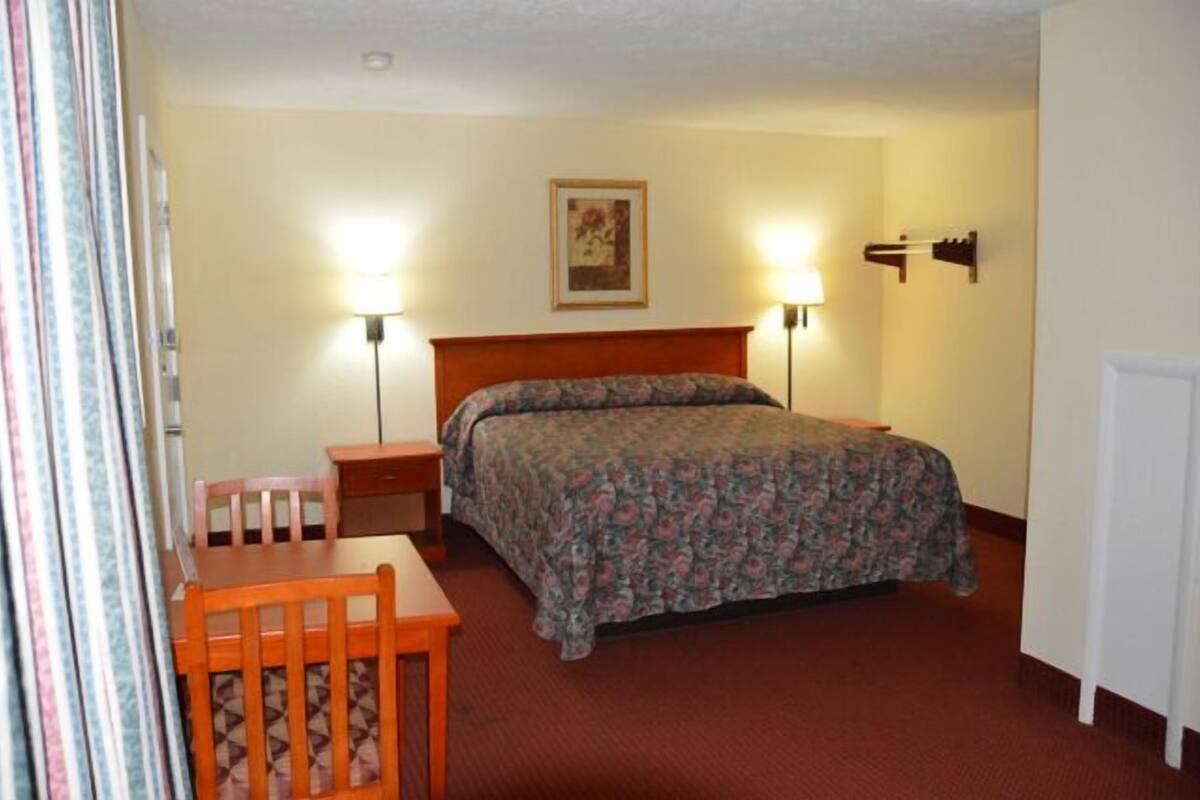 A hotel room with a bed, two bedside tables, a desk with a chair, and two wall-mounted lamps.
