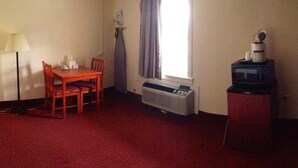 A hotel room with a wooden table, a chair, a lamp, an air conditioner, a television on a cabinet, and a window with curtains. - Crown Inn Motel (Yorktown)