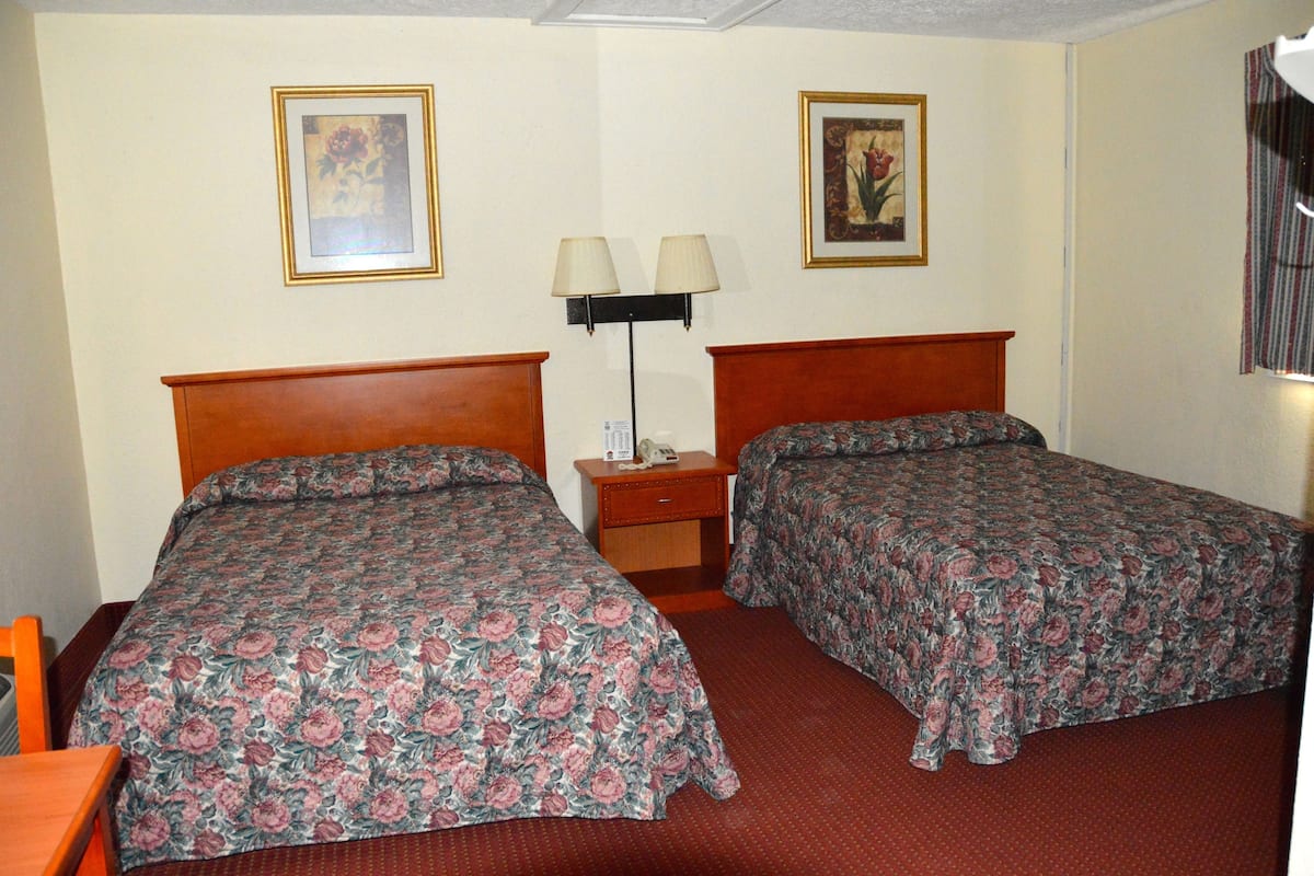 A hotel room with two beds, a nightstand with a lamp, and two framed pictures on the wall.