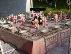 Une table dressée pour un événement formel en plein air, avec des serviettes roses, des assiettes blanches et de la verrerie transparente.