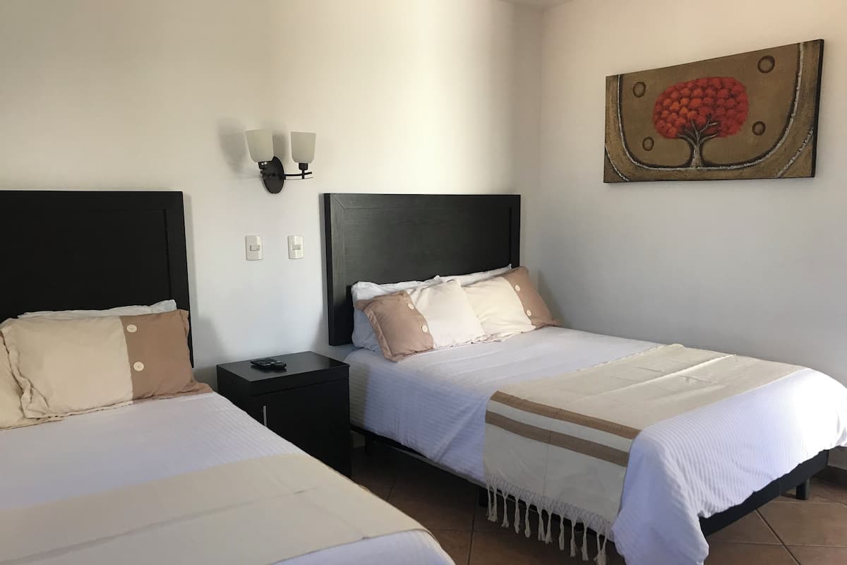 Camera d'albergo con due letti, un comodino, un punto luce a parete e un quadro.