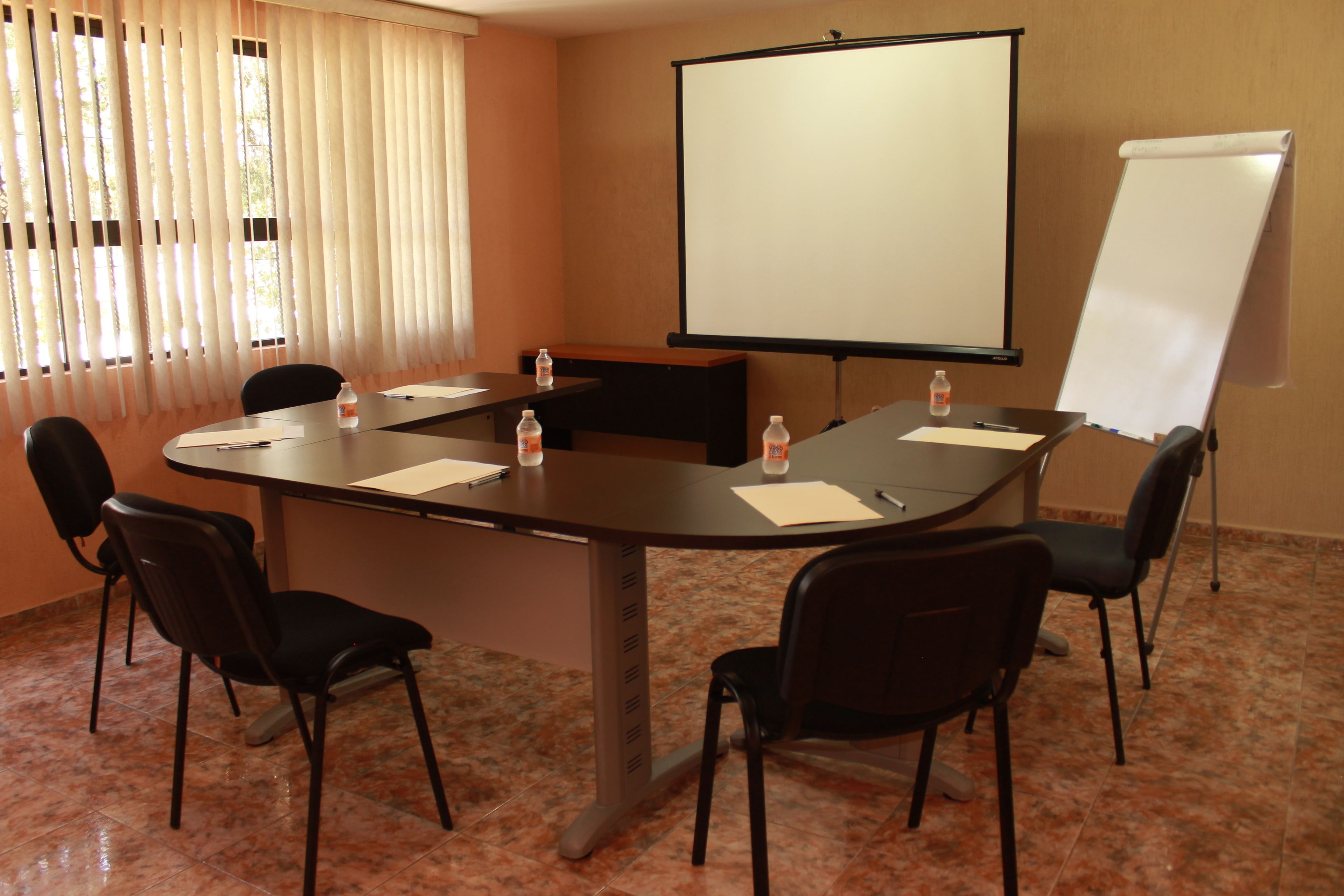 A conference room with a large table, four chairs, a projector screen, and a whiteboard.