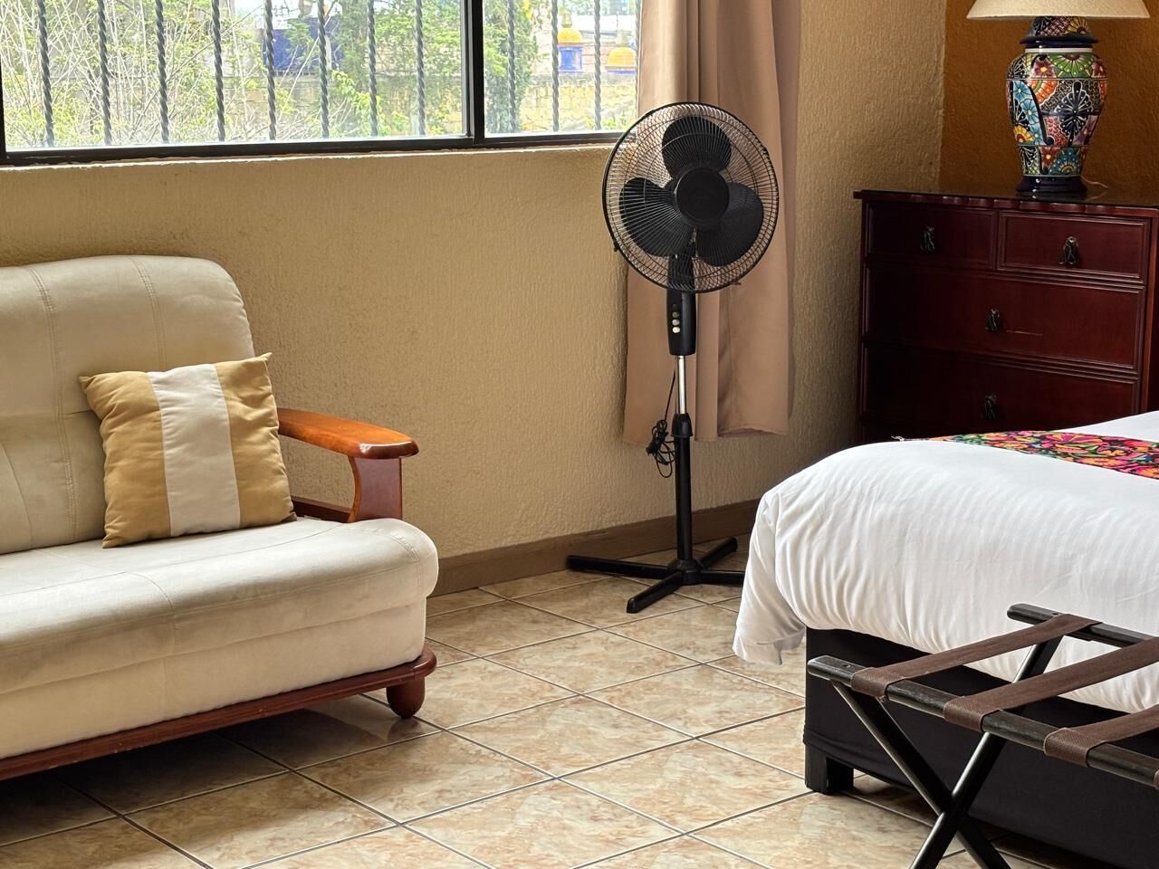 A hotel room with a sofa, a standing fan, a bed, and a dresser.