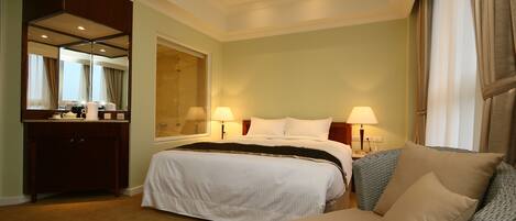 Habitación de hotel con una cama grande, dos mesitas de noche con lámparas, un aparador y un espejo amplio.