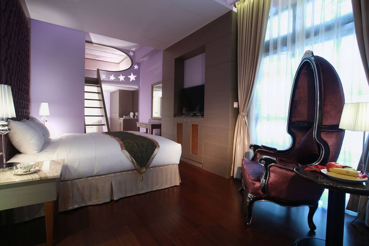 A hotel room with a bed, a vanity with a mirror, a television, a chair, and a window with curtains.