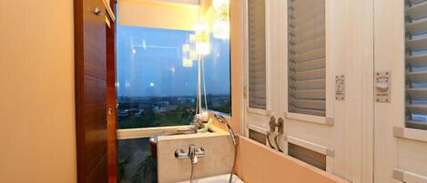 A bathroom with a bathtub, a window with blinds, and a view of the cityscape.