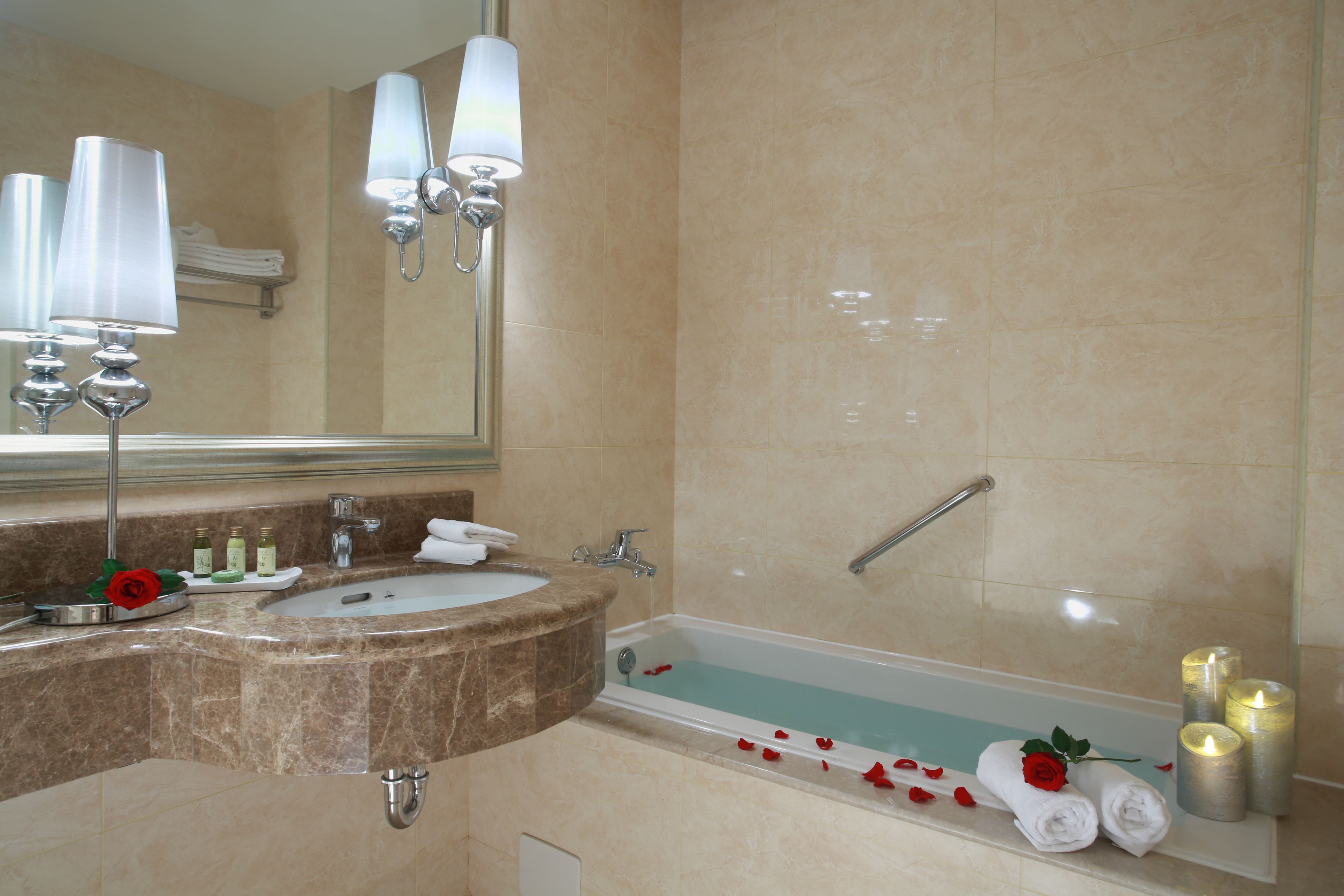 Une salle de bain avec un lavabo, un miroir et une baignoire. On y trouve des bougies et des serviettes sur le bord de la baignoire.