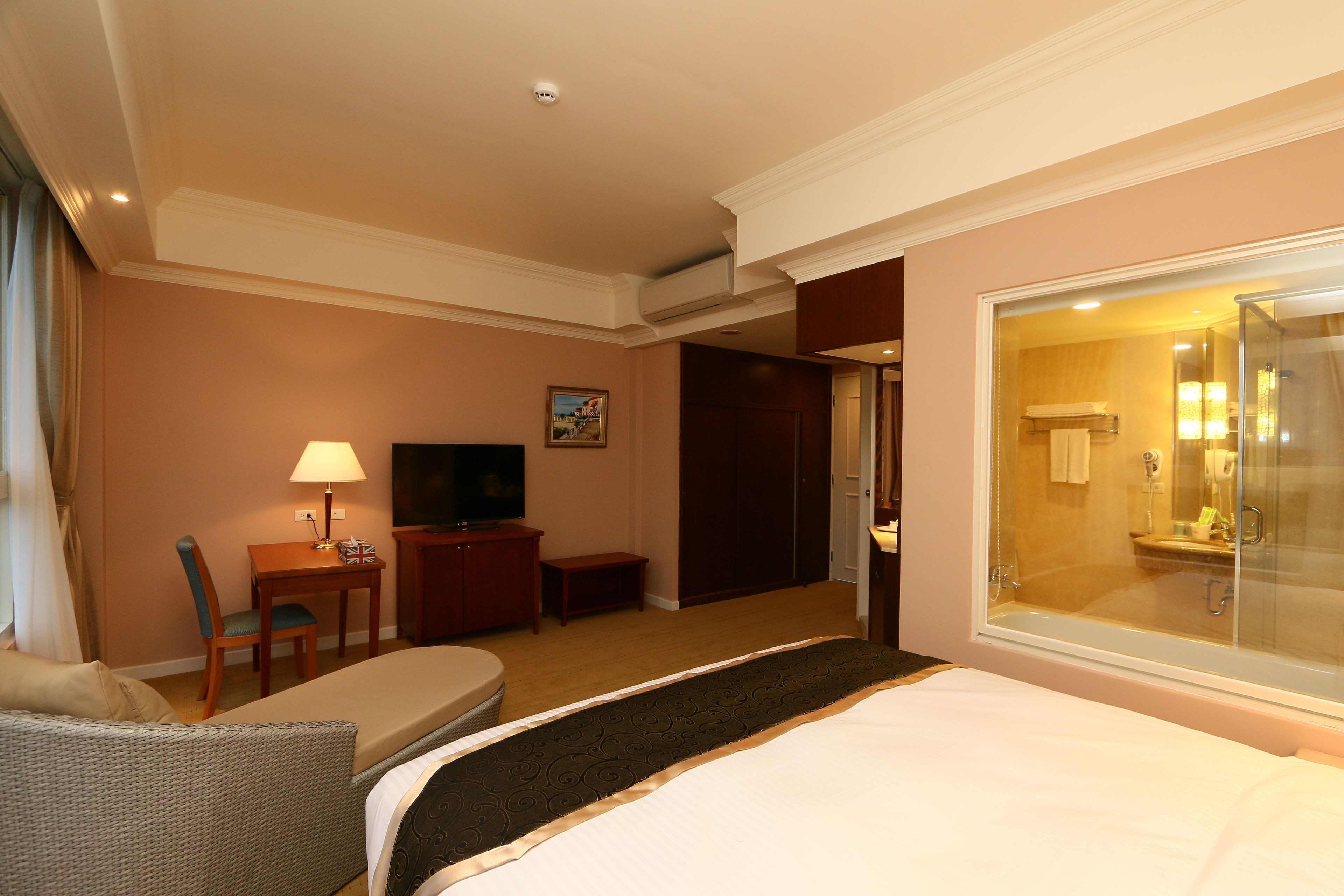 Ein Hotelzimmer mit Bett, Schreibtisch, Stuhl, Fernseher und einem durch eine Glastür sichtbaren Badezimmer.