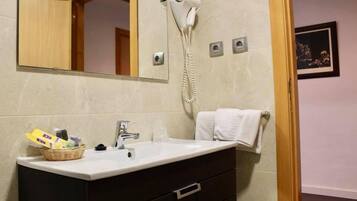 A bathroom with a white sink, dark cabinets, a hairdryer mounted on the wall, and a framed picture on the wall.