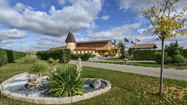 A building with a tower, surrounded by a landscaped garden with a circular stone feature. - Motel Cancun León (Ardon)