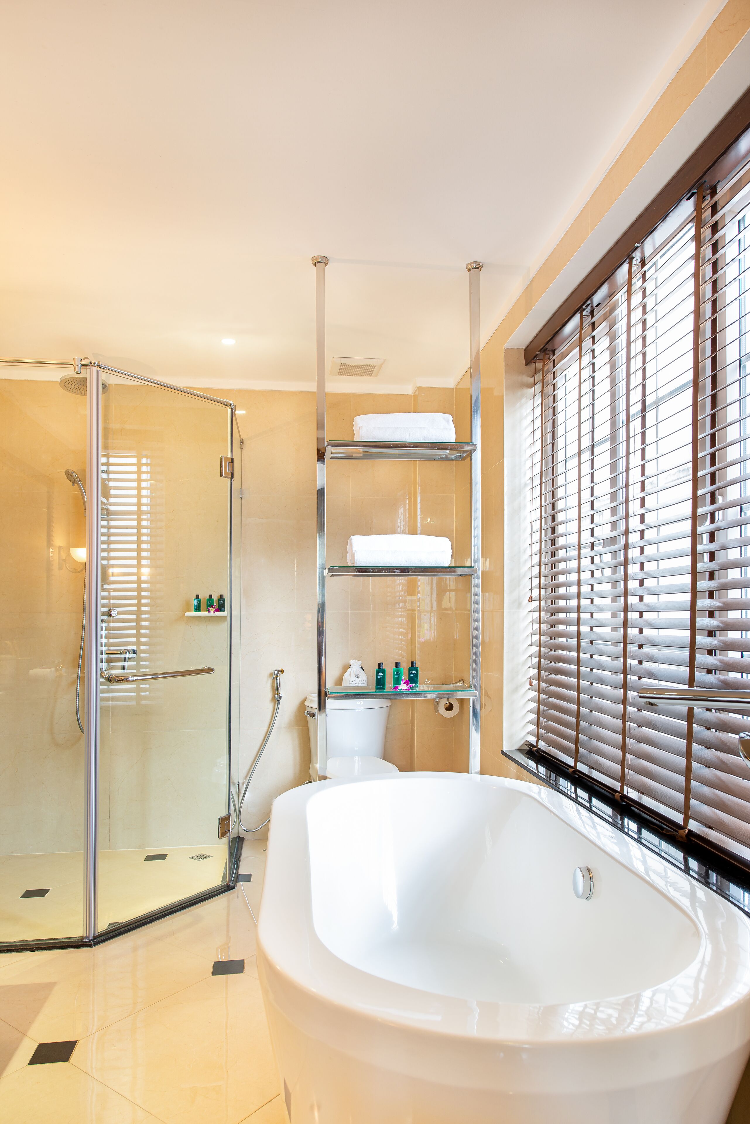 A modern bathroom with a glass-enclosed shower, a freestanding bathtub, and shelves with toiletries.
