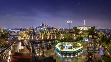 A rooftop bar with a view of the city skyline, a bridge, and a sign for 'MOONLIGHT SKY BAR'.