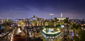 A rooftop bar with a view of the city skyline, a bridge, and a sign for 'MOONLIGHT SKY BAR'.