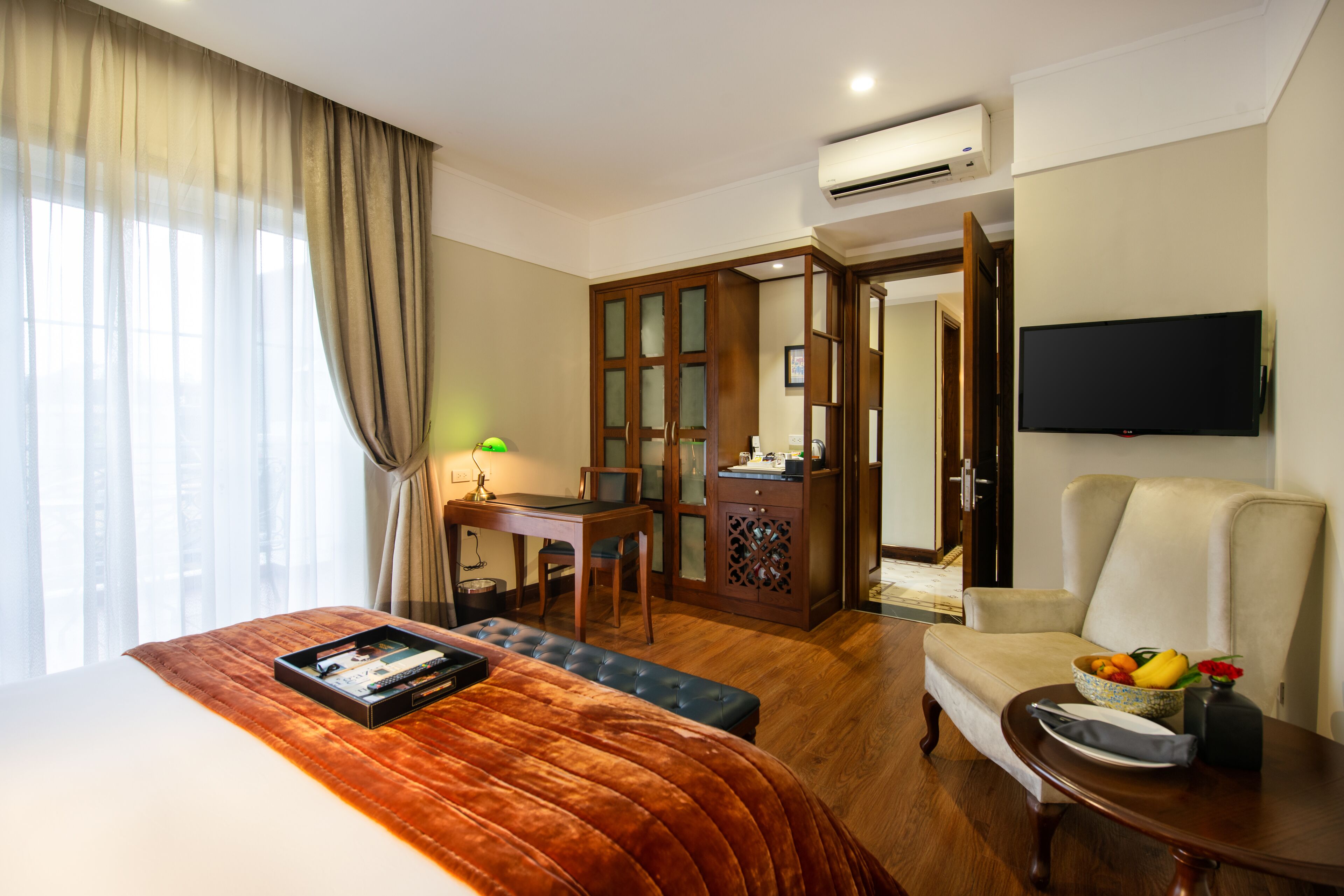 Habitación de hotel con cama, escritorio, silla, televisor y mesa de comedor con un bol de fruta.